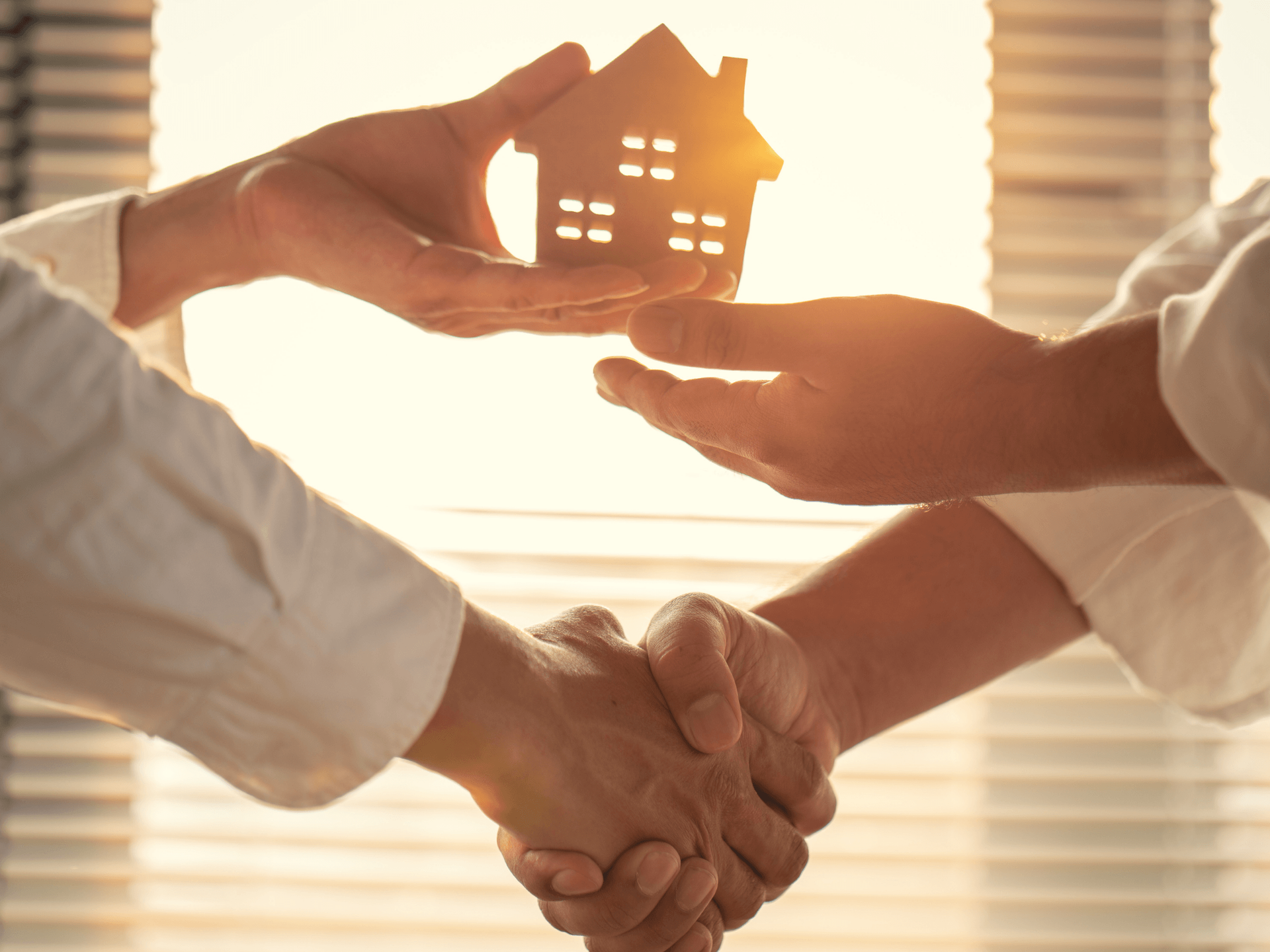 Hands exchanging a small house model during a handshake, symbolizing trust and protection from a home and auto insurance broker service in Maricopa, AZ