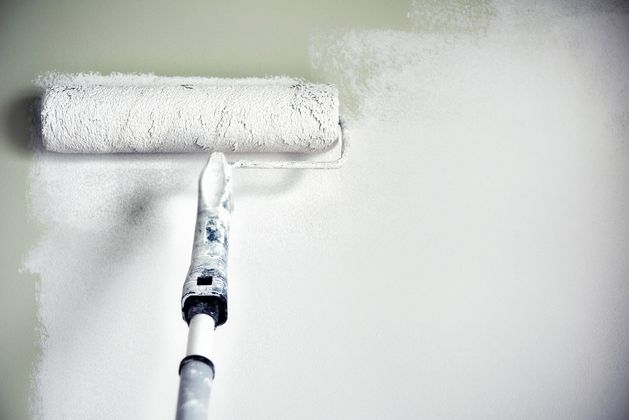 A paint roller is being used to paint a wall white.