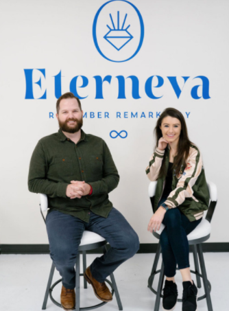 Two people sitting on stools in front of a white wall featuring the blue 