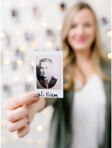 A person holds a small, rectangular photograph of a man labeled 