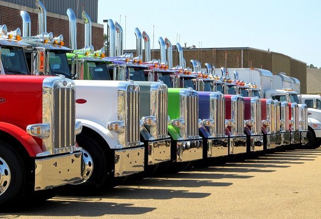 A row of semi trucks are parked in a parking lot