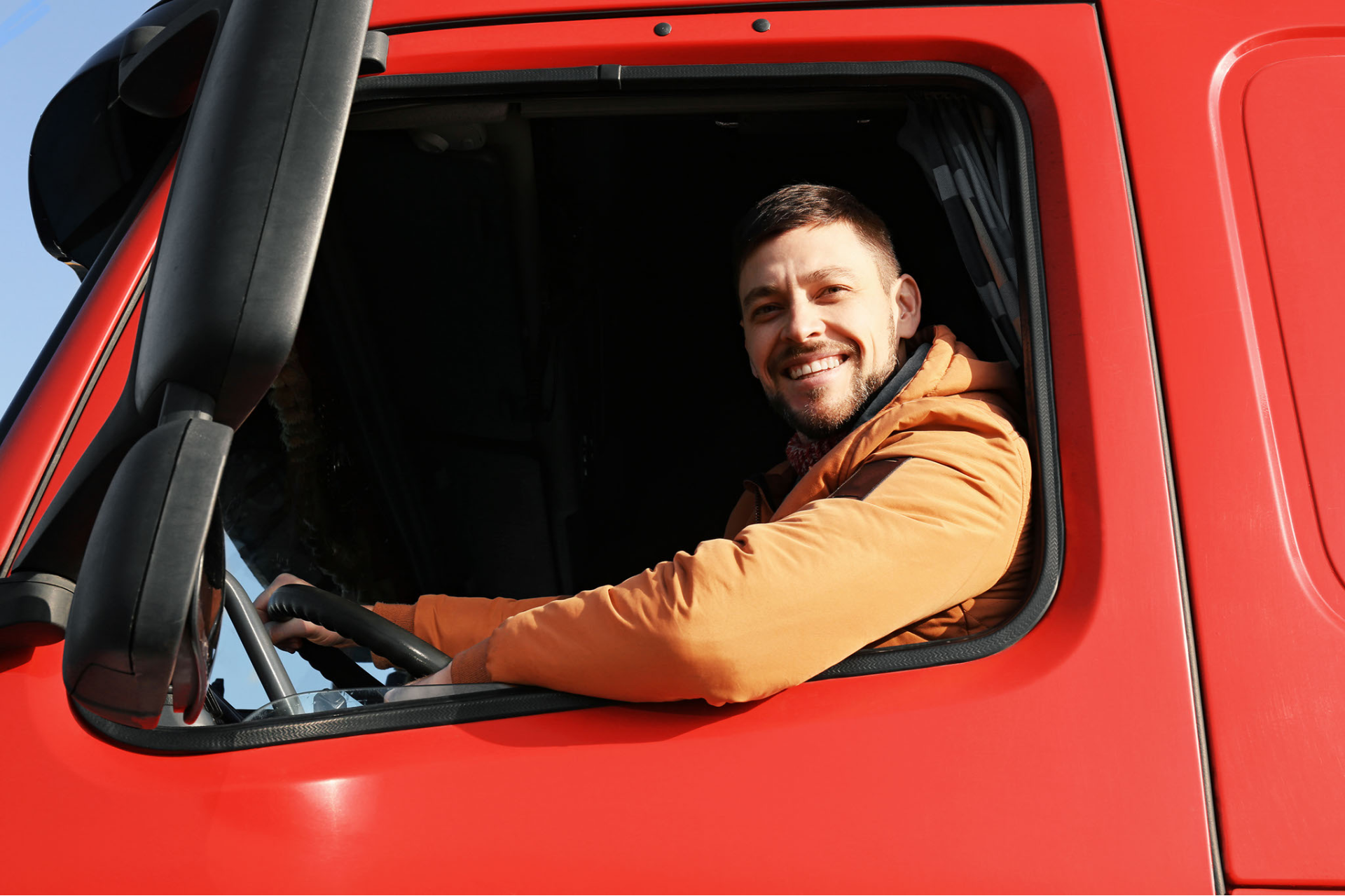 A man is sitting in the driver 's seat of a red truck.