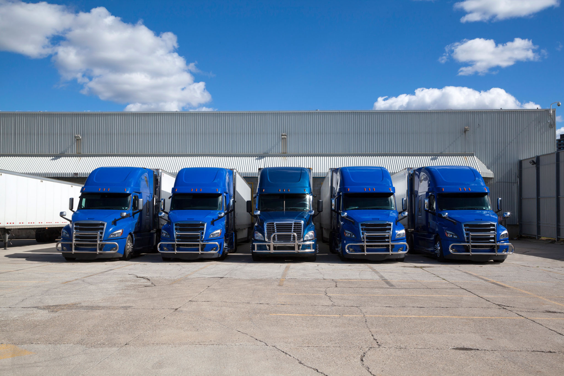 A row of blue semi trucks are parked in front of a building.