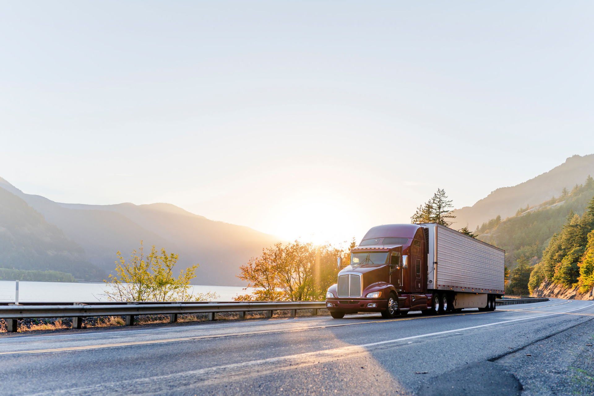 A semi truck is driving down a highway next to a lake at sunset.