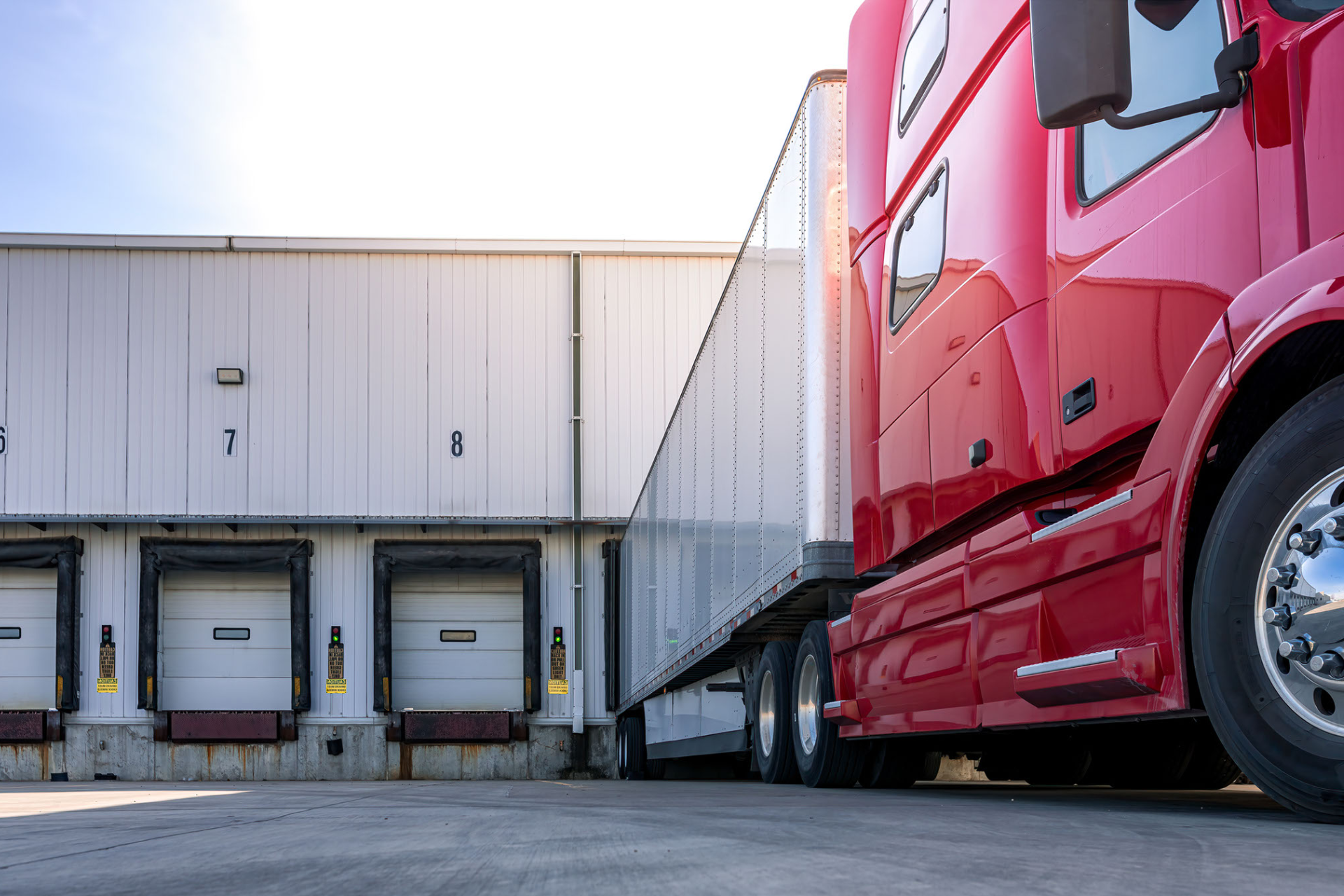 A red semi truck is parked in front of a warehouse.