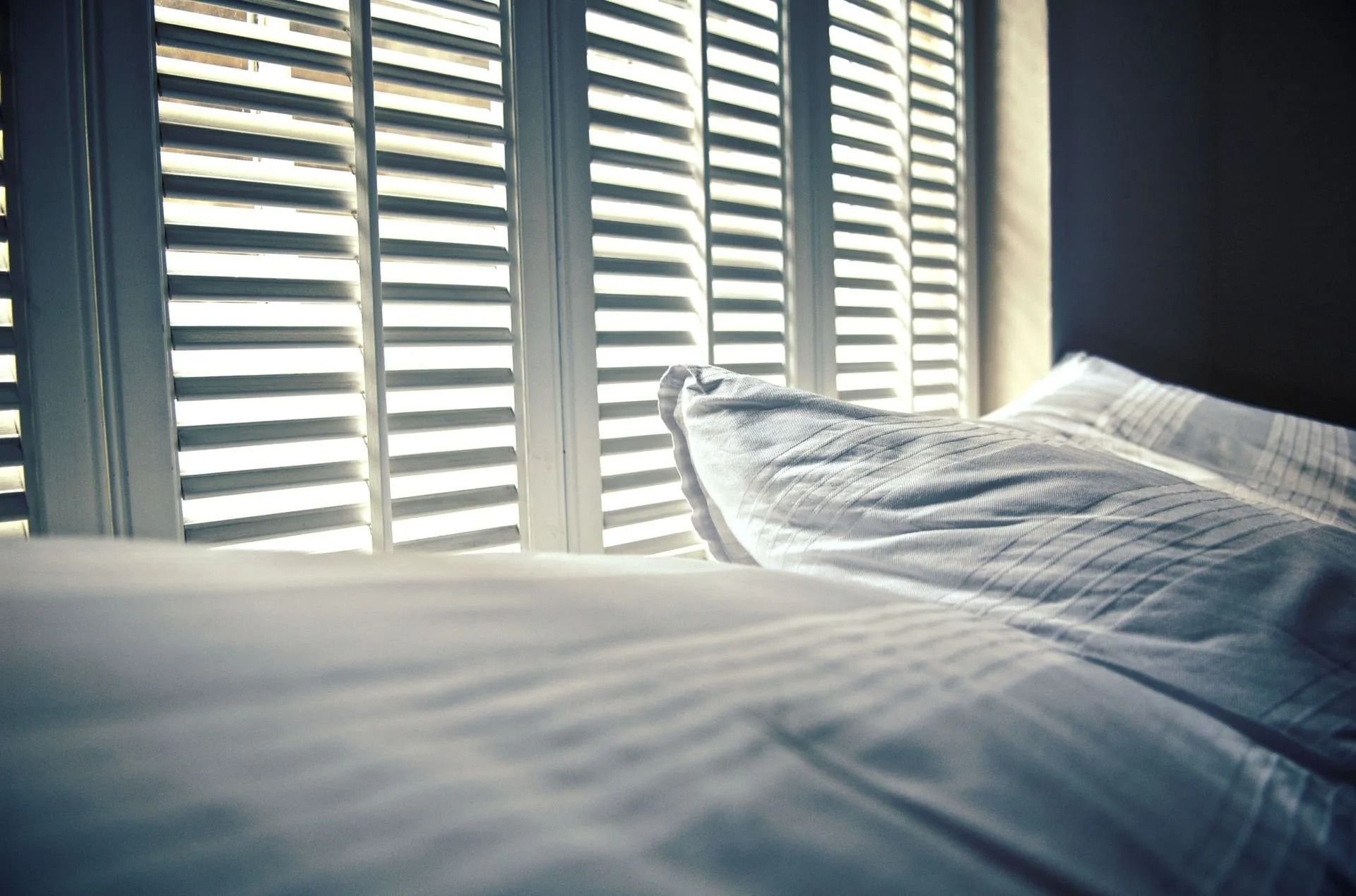 The sun is shining through the window shutters on the bed.