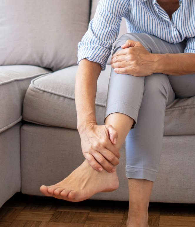 Person sitting on a sofa, holding an ankle as if in pain or injury