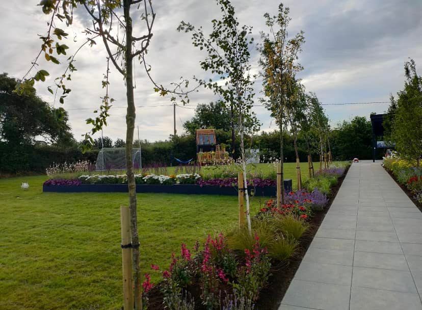A walkway leading to a lush green field with flowers and trees.