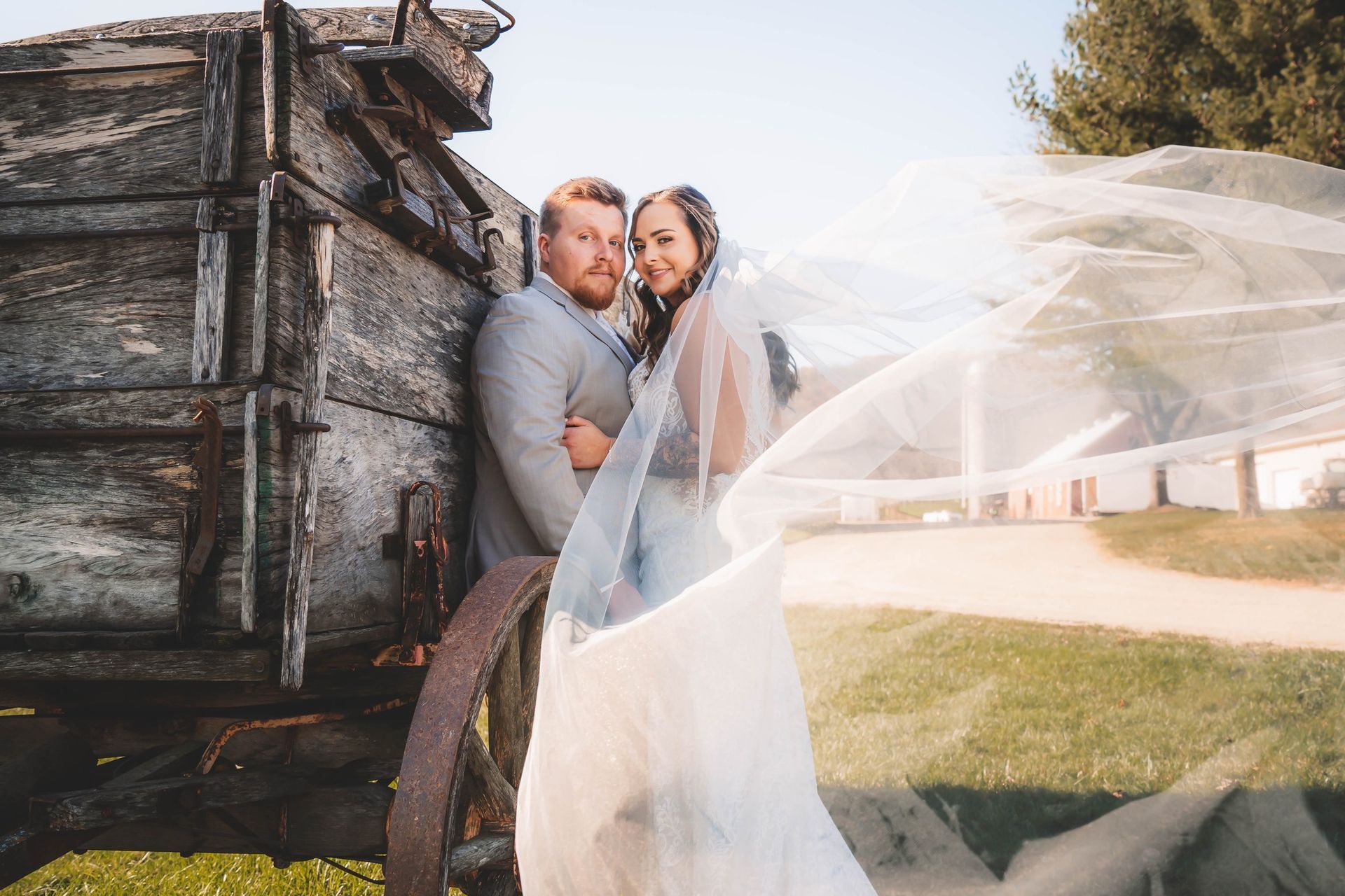 A bride and groom are posing for a picture in front of an old wooden wagon. A bride and groom are posing for a picture in front of an old wooden wagon.