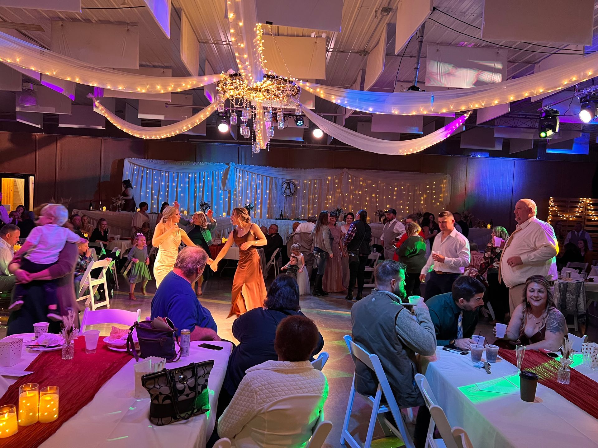A group of people are dancing in a large room at a wedding reception. A group of people are dancing in a large room at a wedding reception.