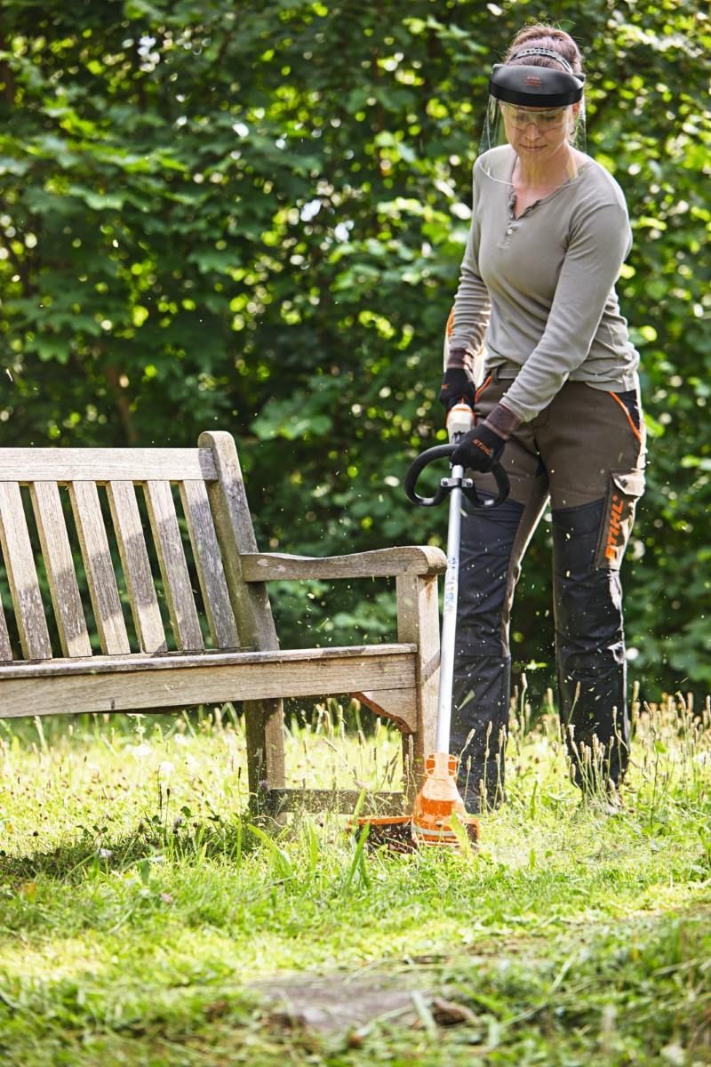 A Woman is Mowing the Grass in Front of a Wooden Bench — Jacksons Mower Centre in Mackay, QLD