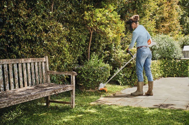 A Woman is Using a Lawn Mower in a Garden Next to a Bench — Jacksons Mower Centre in Mackay, QLD