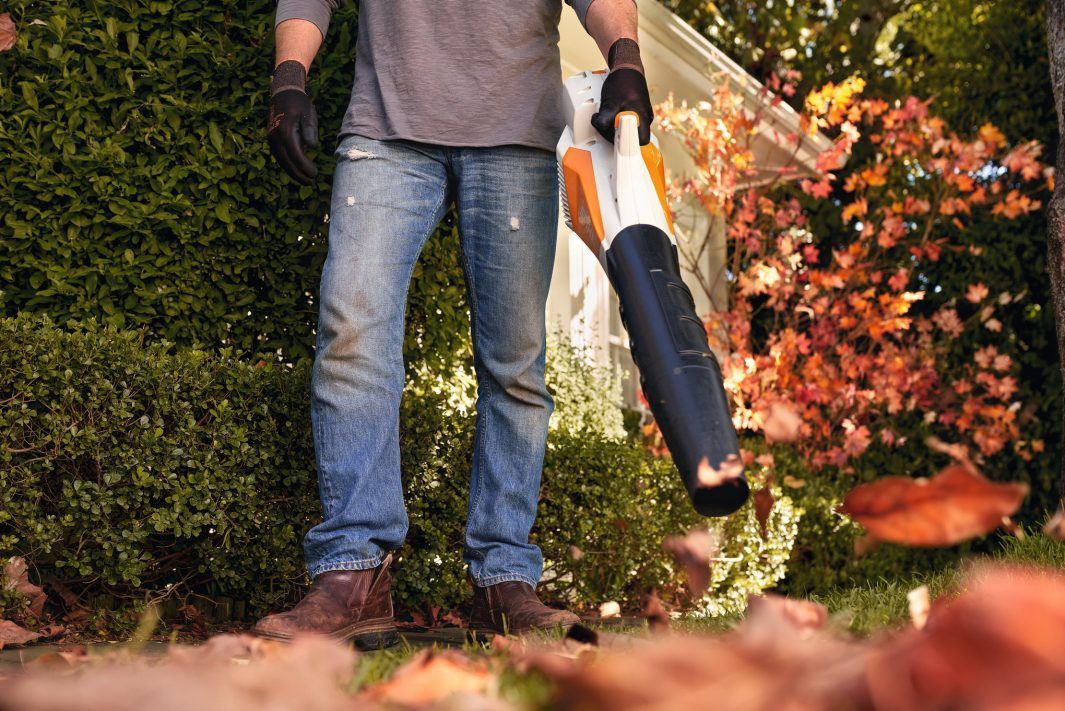 A Man is Blowing Leaves in a Garden With a Blower — Jacksons Mower Centre in Mackay, QLD