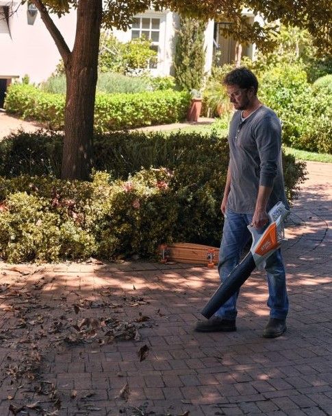 A Man is Blowing Leaves on a Brick Sidewalk — Jacksons Mower Centre in Mackay, QLD