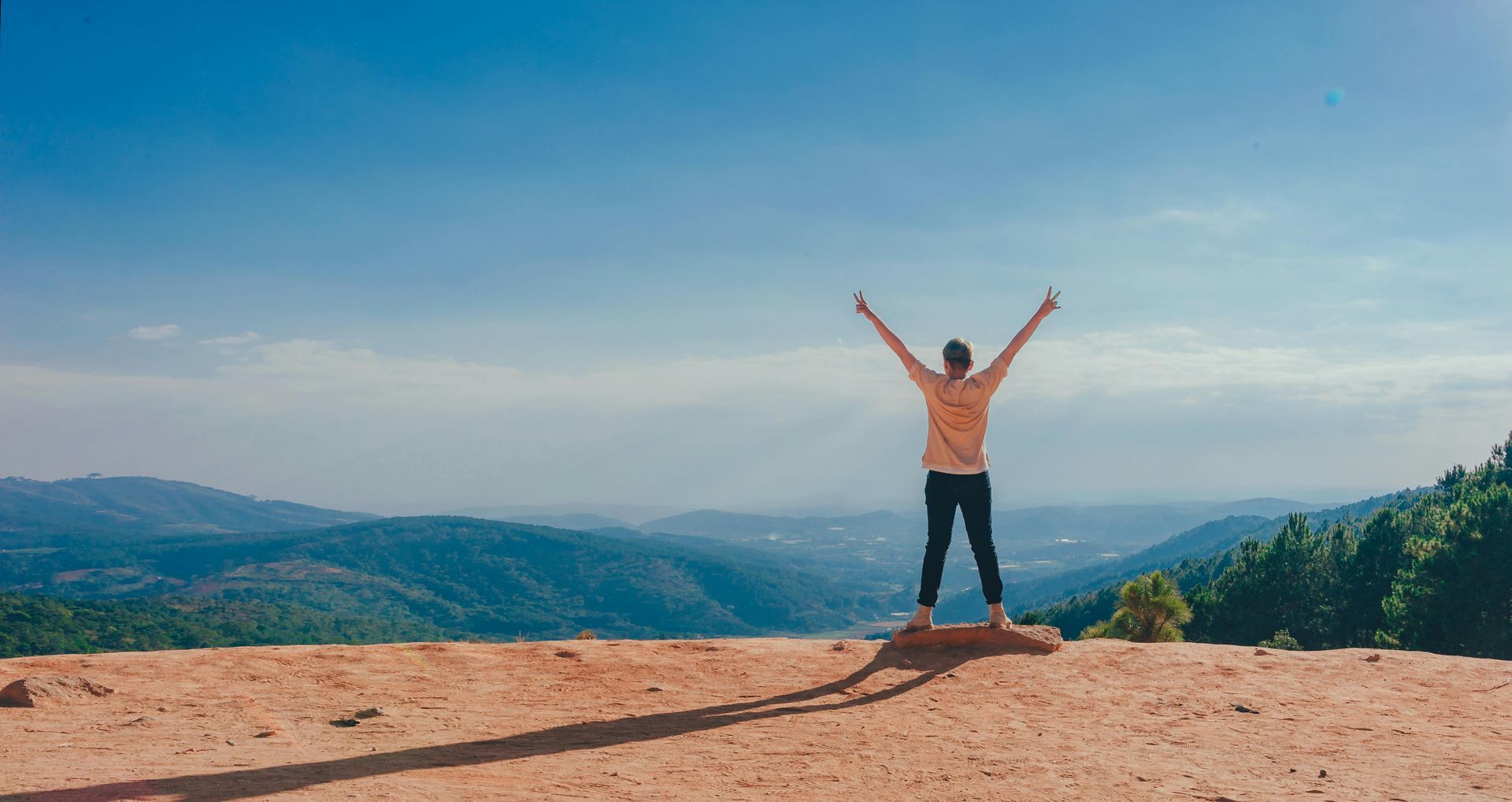 A woman is standing on top of a mountain with her arms in the air. Wed Design