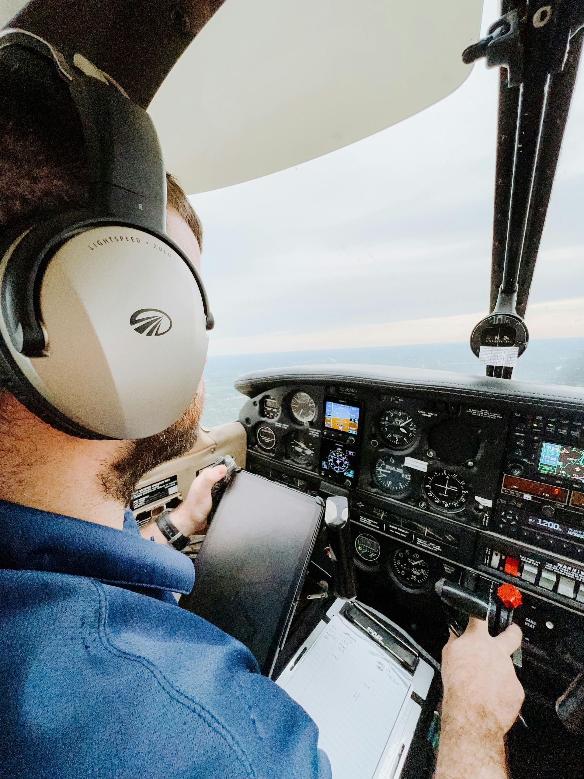 Pilot in cockpit wearing headset, flying an aircraft and monitoring the instrument panel.
