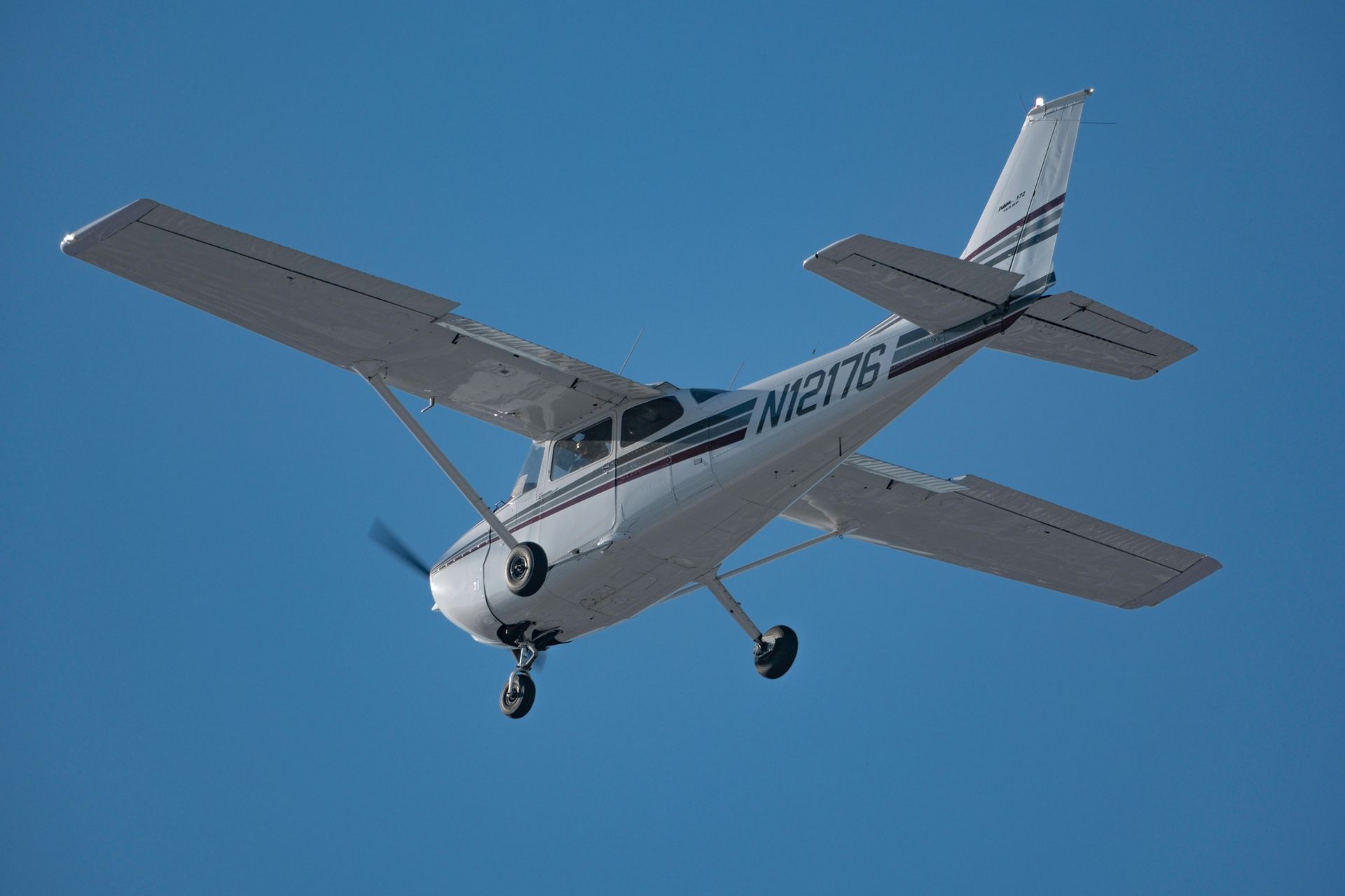 Small white single-engine airplane flying against a clear blue sky.