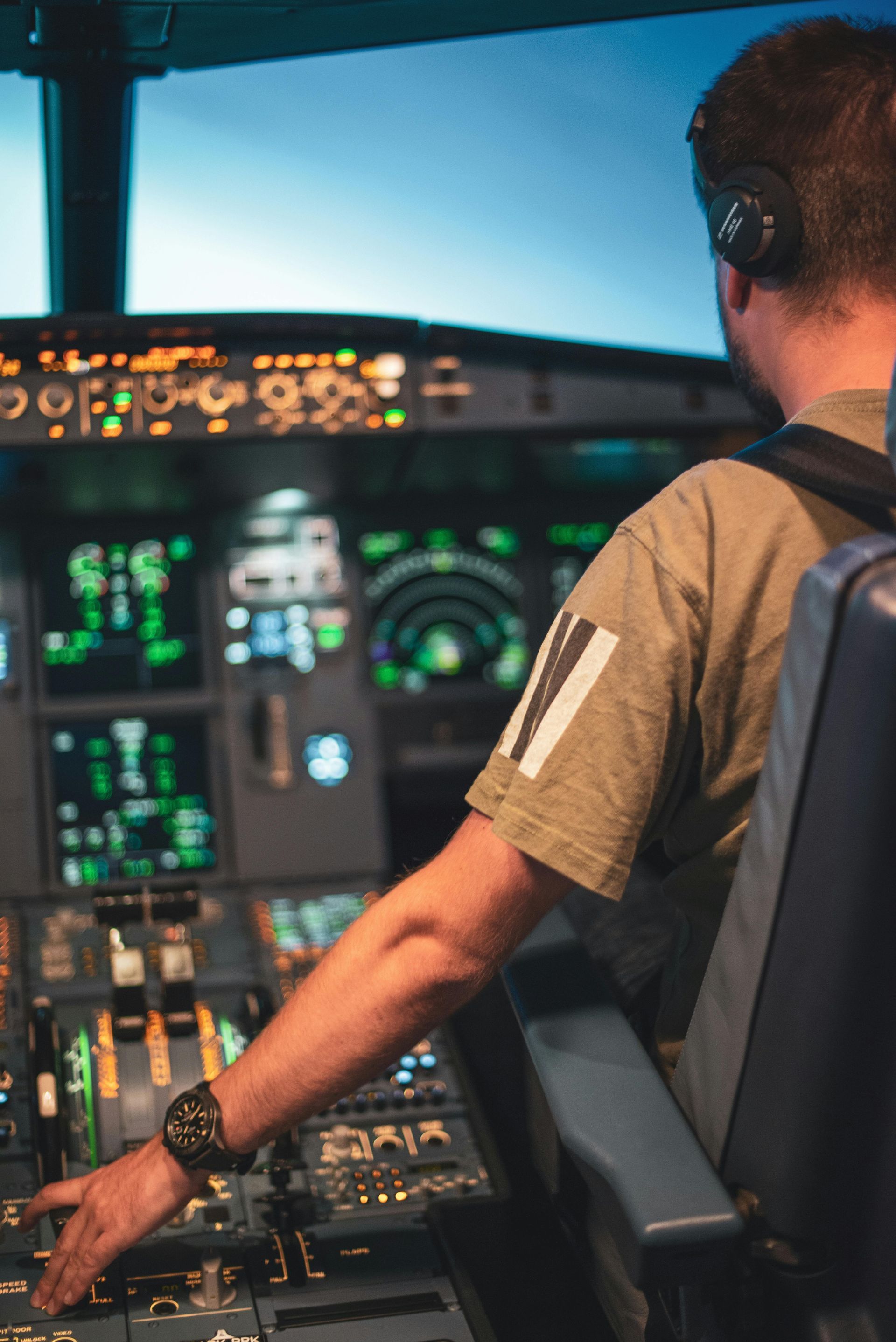 Pilot in headset seated in an airplane cockpit, reaching toward the control panel at sunset.