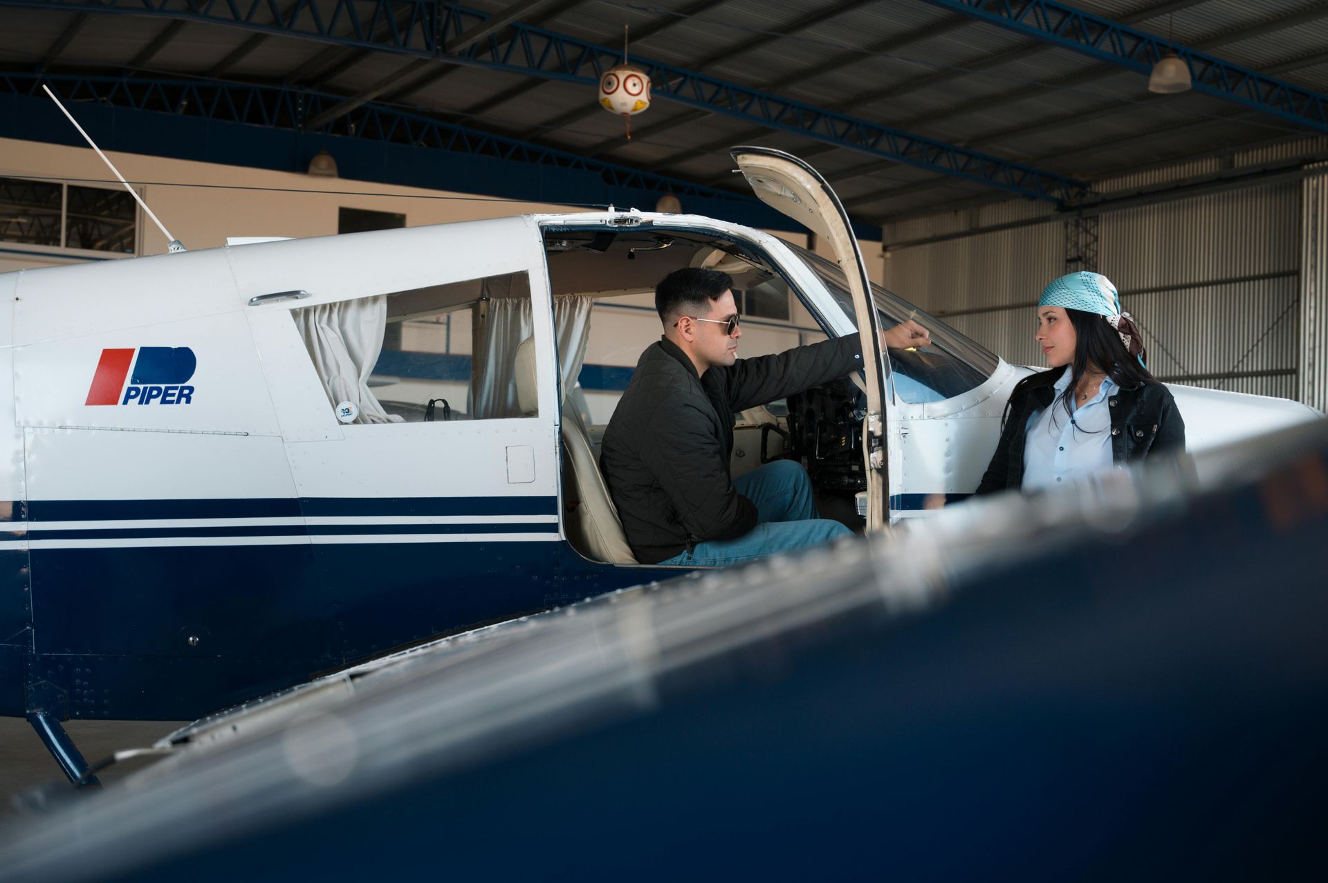 Two people beside a small blue-and-white airplane inside a hangar