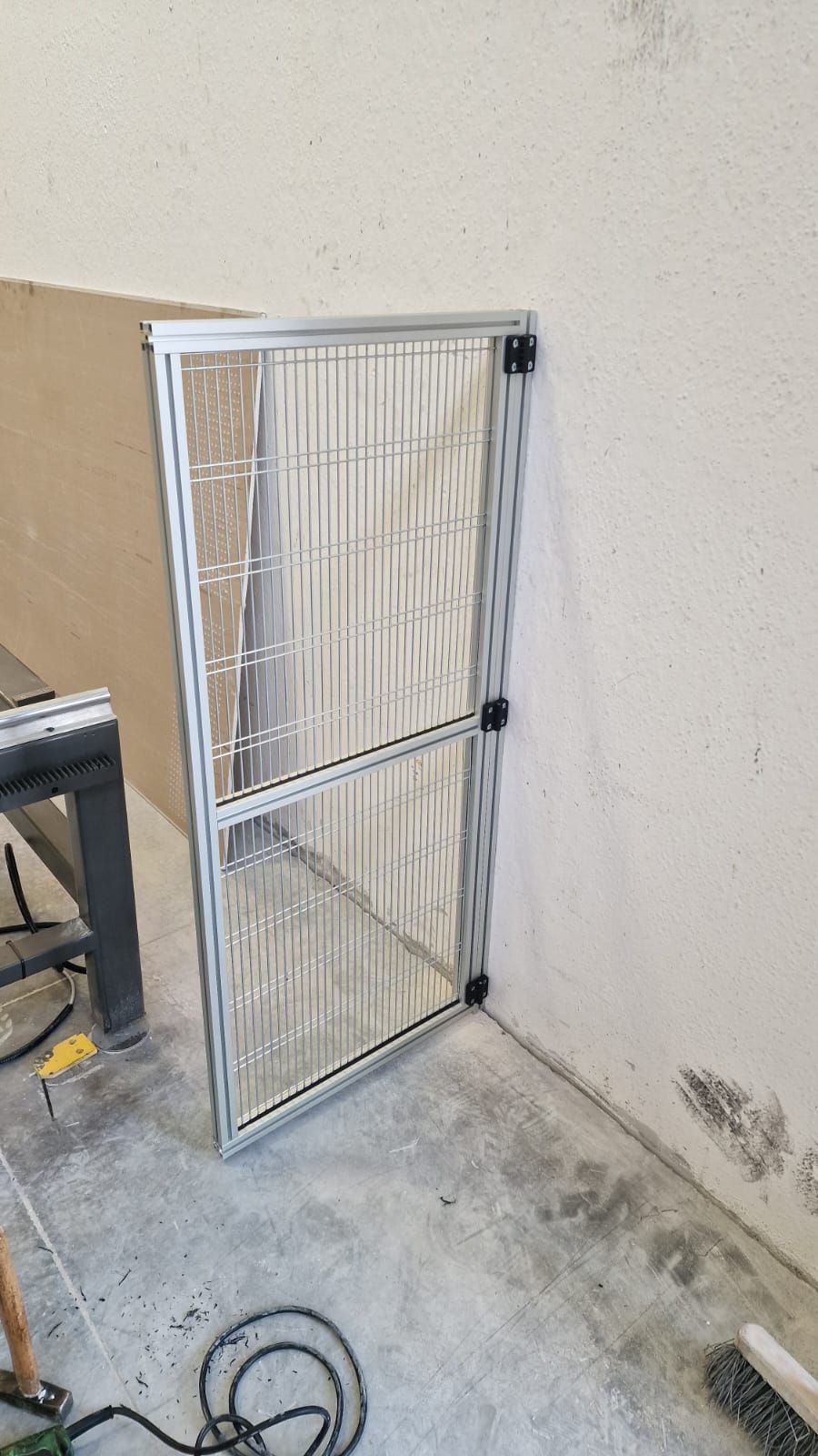 Una porta a zanzariera in alluminio di nuova costruzione appoggiata a un muro di cemento all'interno.
