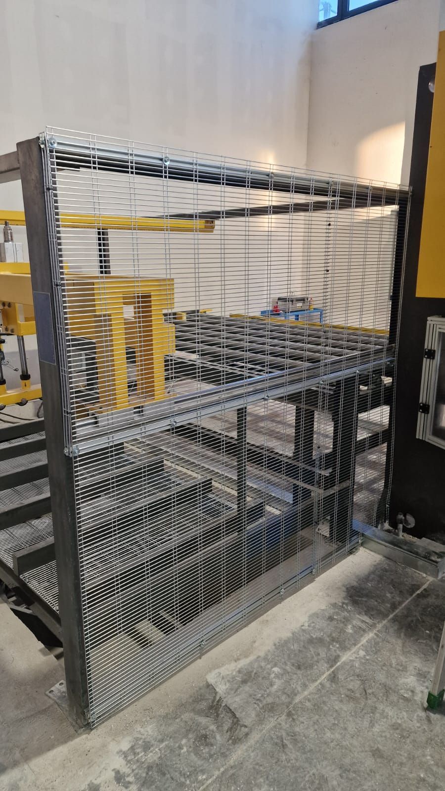 Gabbia di sicurezza in metallo che circonda i macchinari in una fabbrica o in un ambiente industriale; tonalità di grigio, nero e giallo.