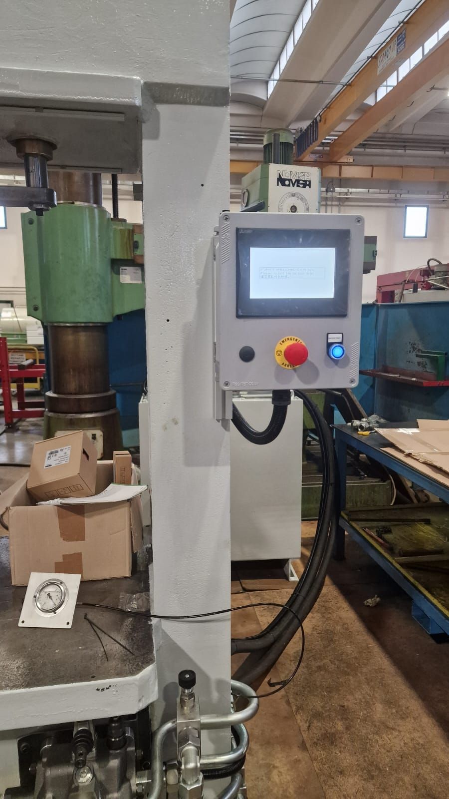 Pannello di controllo installato su una grande pressa industriale in un ambiente di fabbrica, che mostra un pulsante di arresto di emergenza.