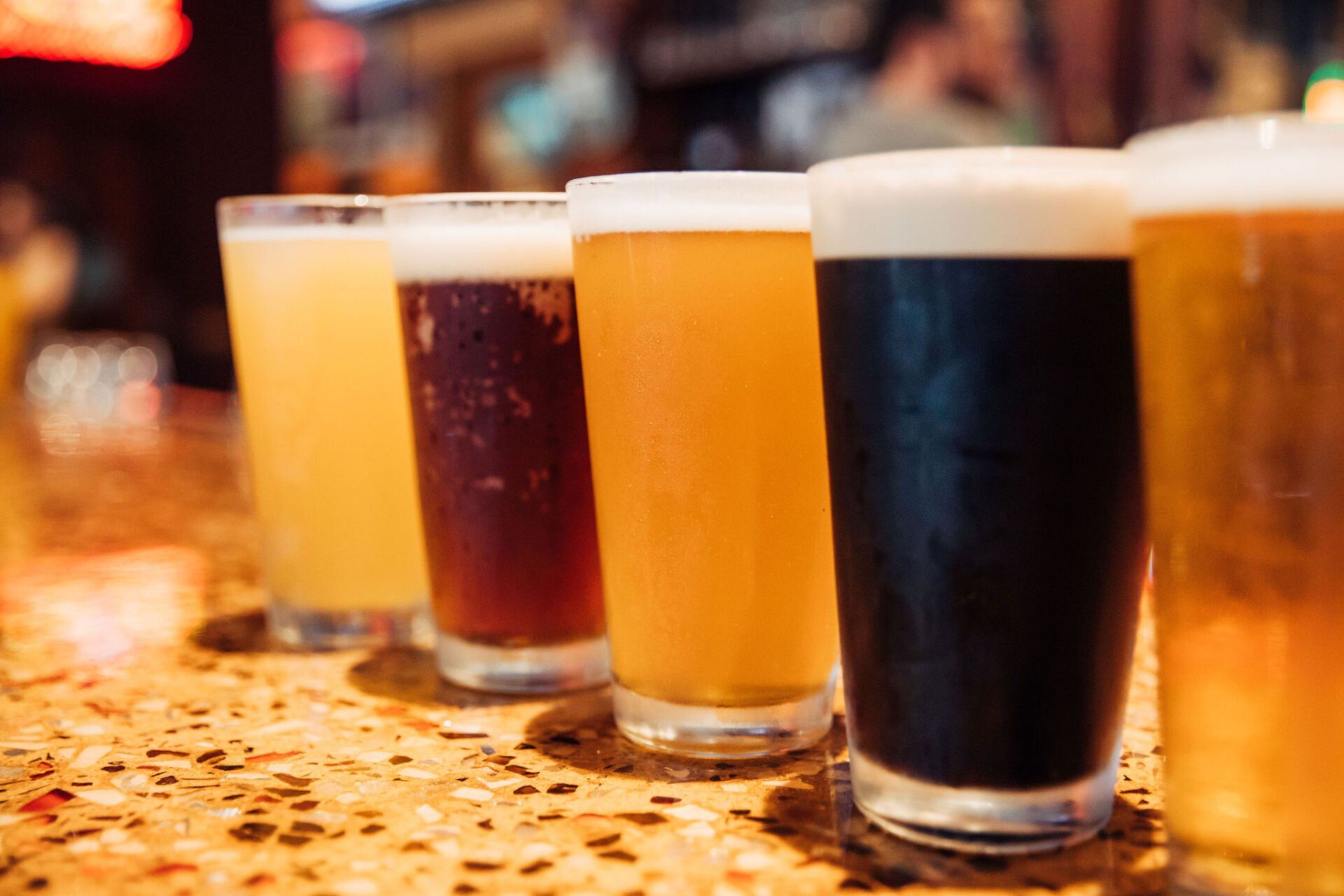 Four different beers in glasses lined up on a bar counter