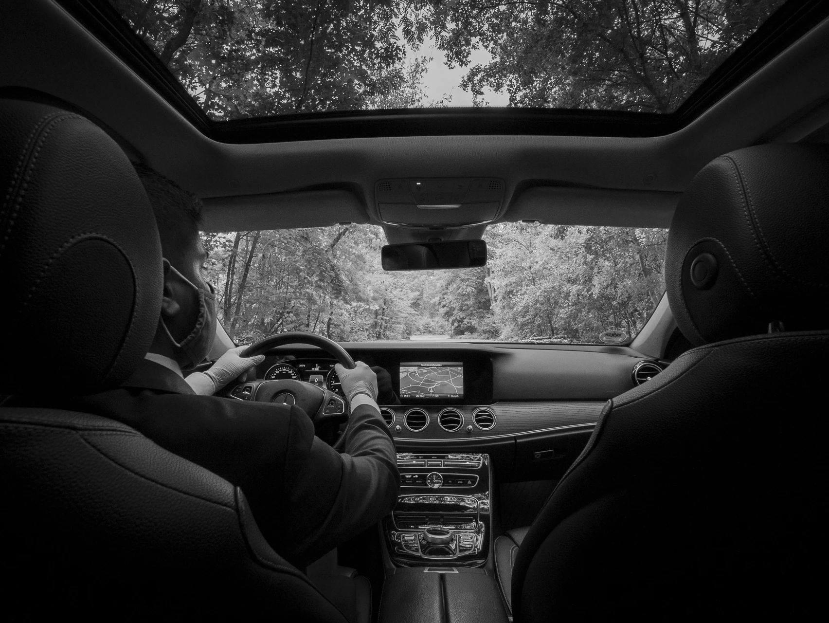 A black and white photo of a man driving a car with a sunroof.