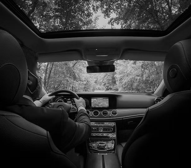 A black and white photo of a man driving a car with a sunroof.