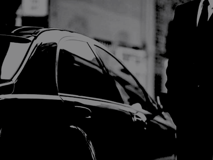 A man in a suit and tie is standing next to a black car.
