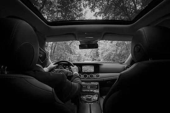 A black and white photo of a man driving a car with a sunroof.