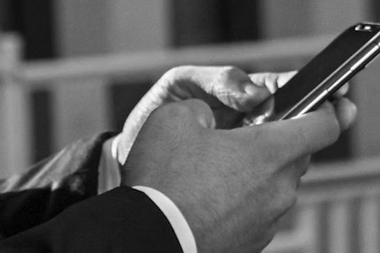 A man in a suit is holding a cell phone in his hand.