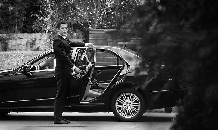 A man in a suit is standing next to a black car.