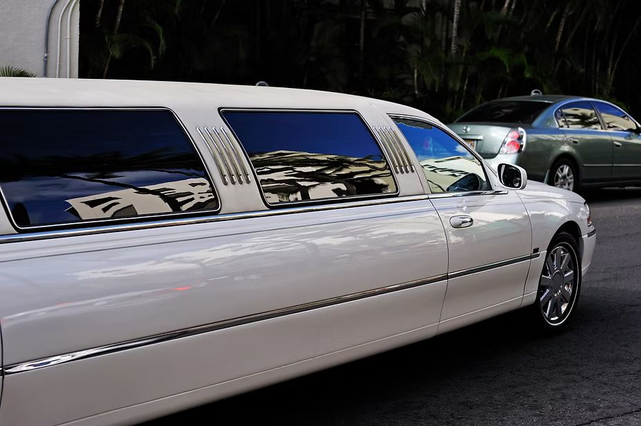 A white limousine is parked next to a green car