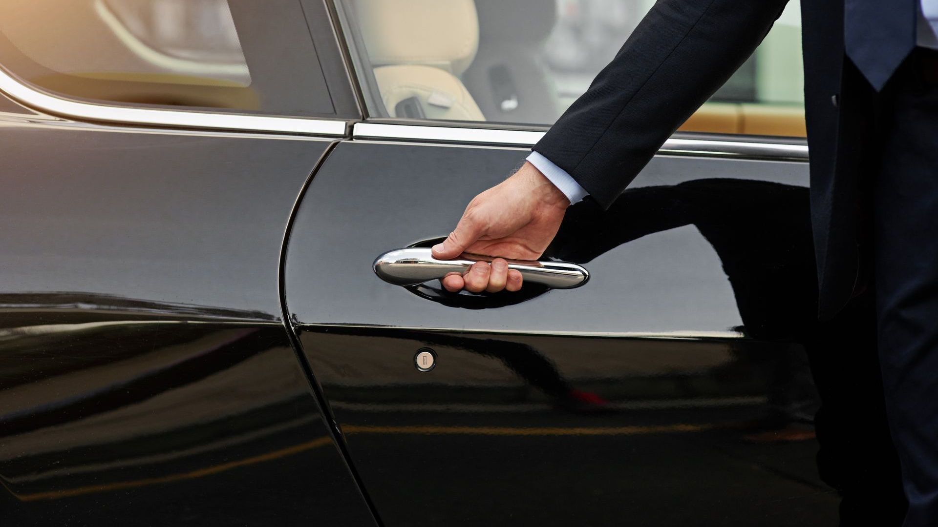 A man in a suit is opening the door of a black car.