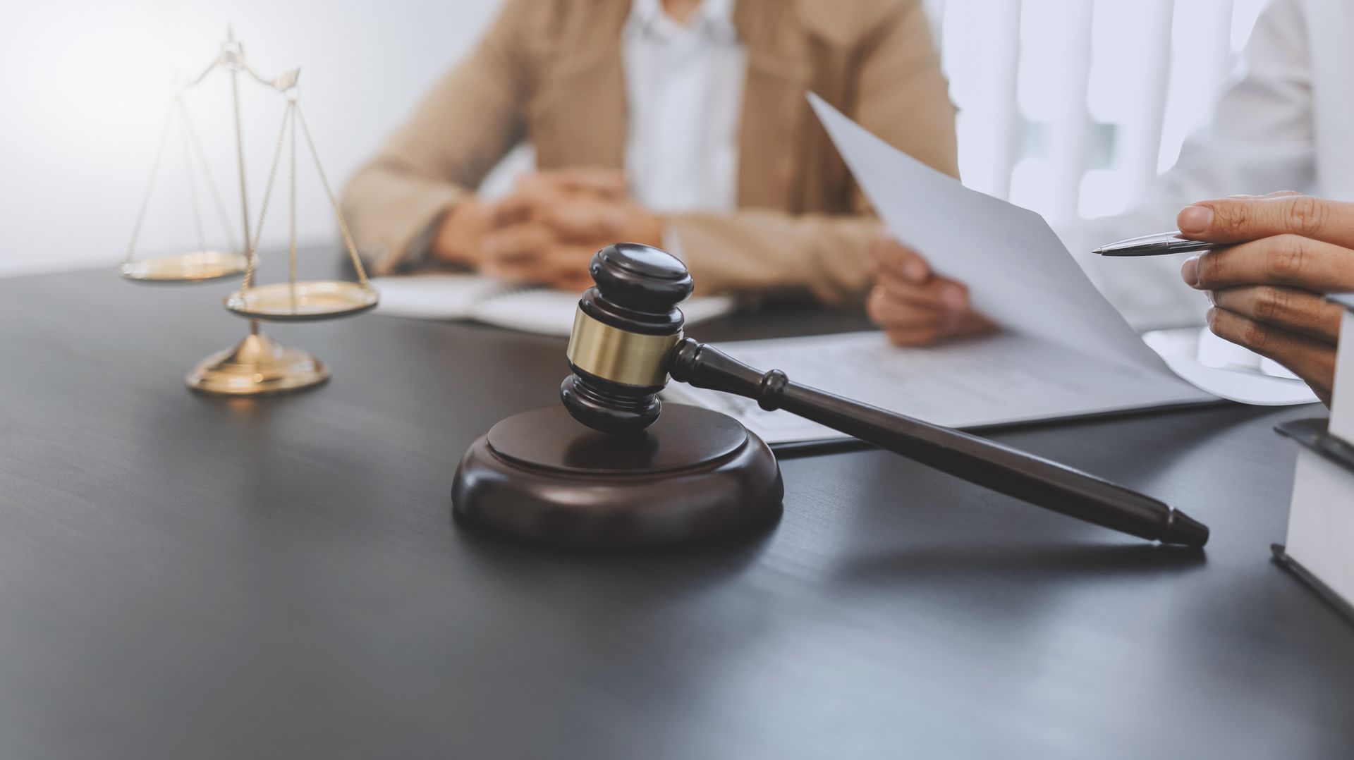 Gavel and scales on a desk as legal professionals review documents during a defense meeting. Gavel and scales on a desk as legal professionals review documents during a defense meeting.