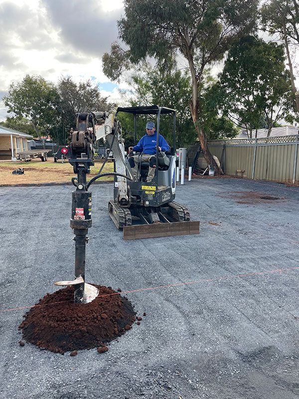 Drilling a Hole in A Gravel-Covered Yard Next to A Pile of Soil — BJB Plumbing & Gasfitting in Cobar, NSW