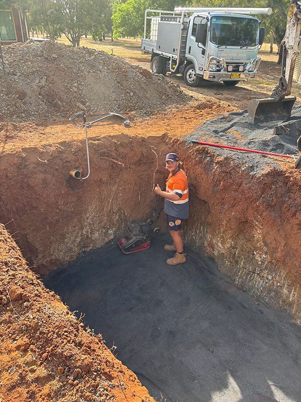 A Man Is Standing in A Hole Next to A Truck — BJB Plumbing & Gasfitting in Dubbo, NSW