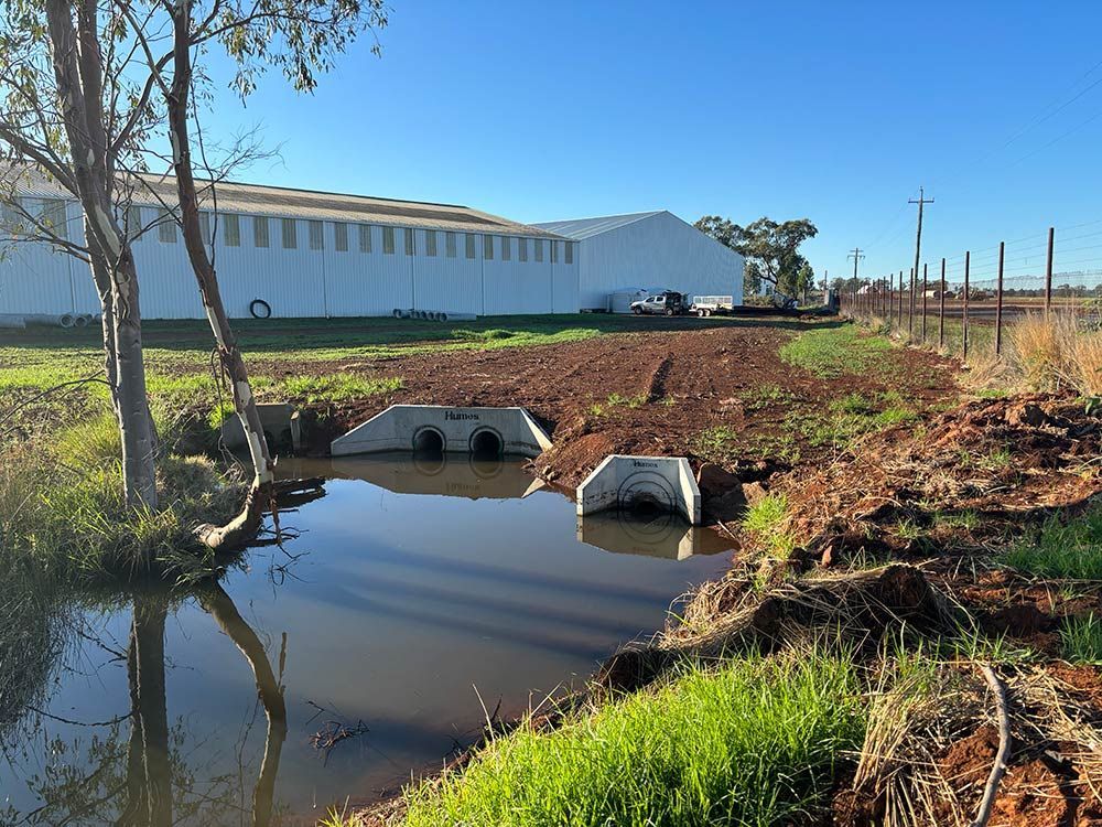 A River Runs Through a Field with A White Building in The Background — BJB Plumbing & Gasfitting in Bourke, NSW