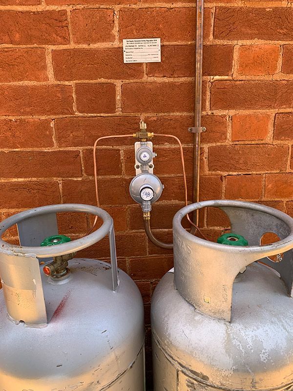 Two Gas Cylinders Are Sitting Next To Each Other On A Brick Wall — BJB Plumbing & Gasfitting in Dubbo, NSW