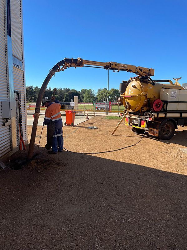 A Man Is Standing Next To A Vacuum Truck In A Parking Lot — BJB Plumbing & Gasfitting in Dubbo, NSW