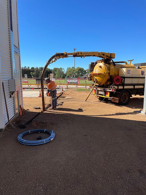 A Man Is Working on A Pipe Next to A Vacuum Truck — BJB Plumbing & Gasfitting in Bourke, NSW