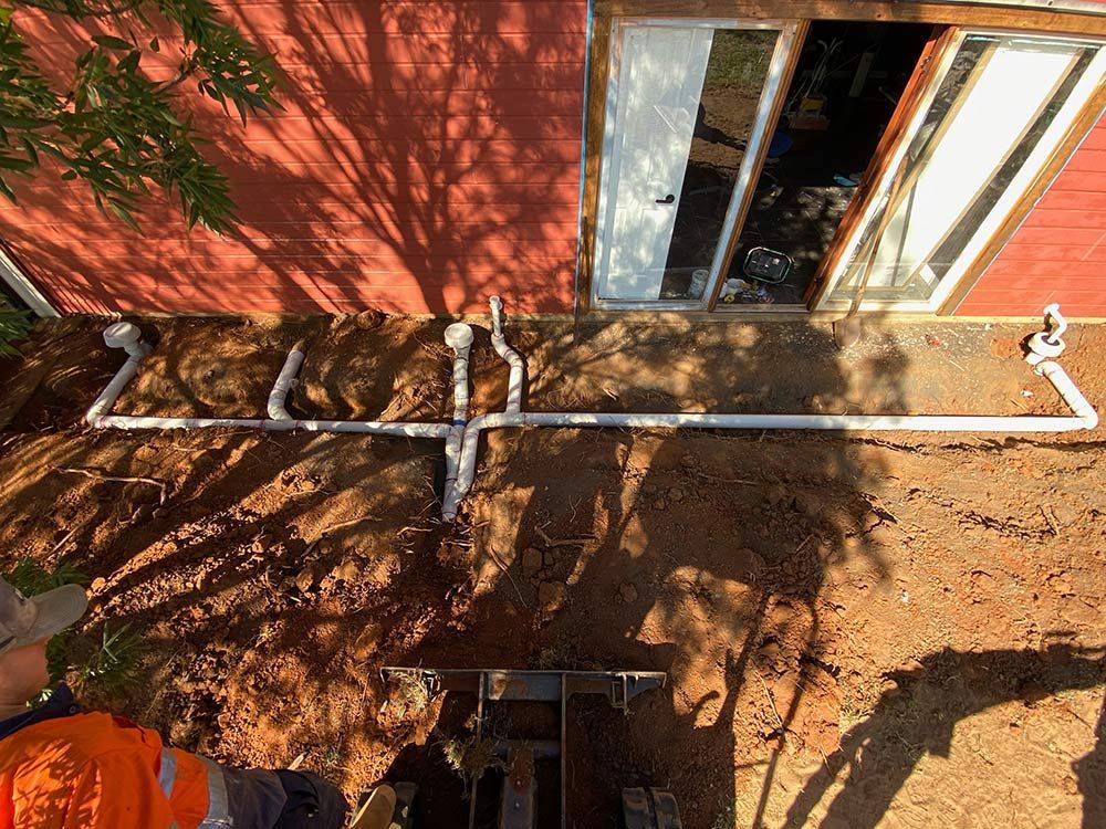 A Man Is Digging a Hole in The Ground in Front of A House — BJB Plumbing & Gasfitting in Bourke, NSW