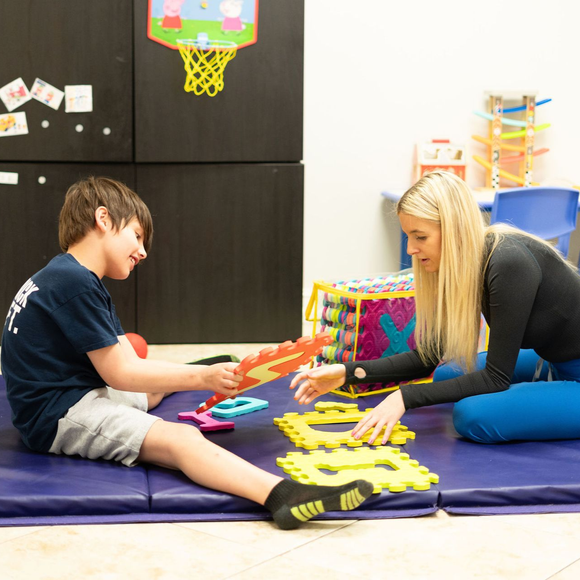 Two children playing a board game on a padded floor in a classroom.