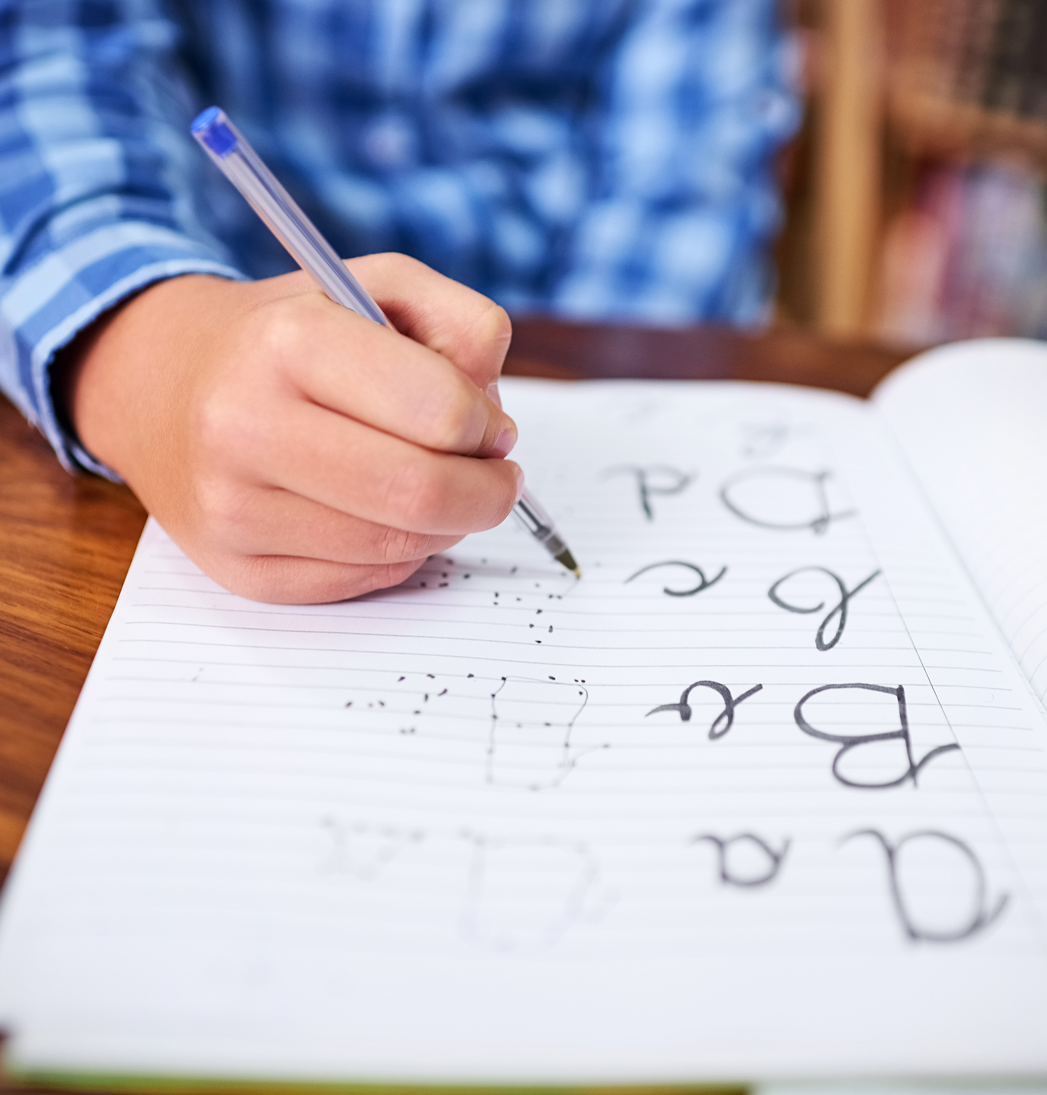 Hand holding a pencil, writing letters in a workbook on a table