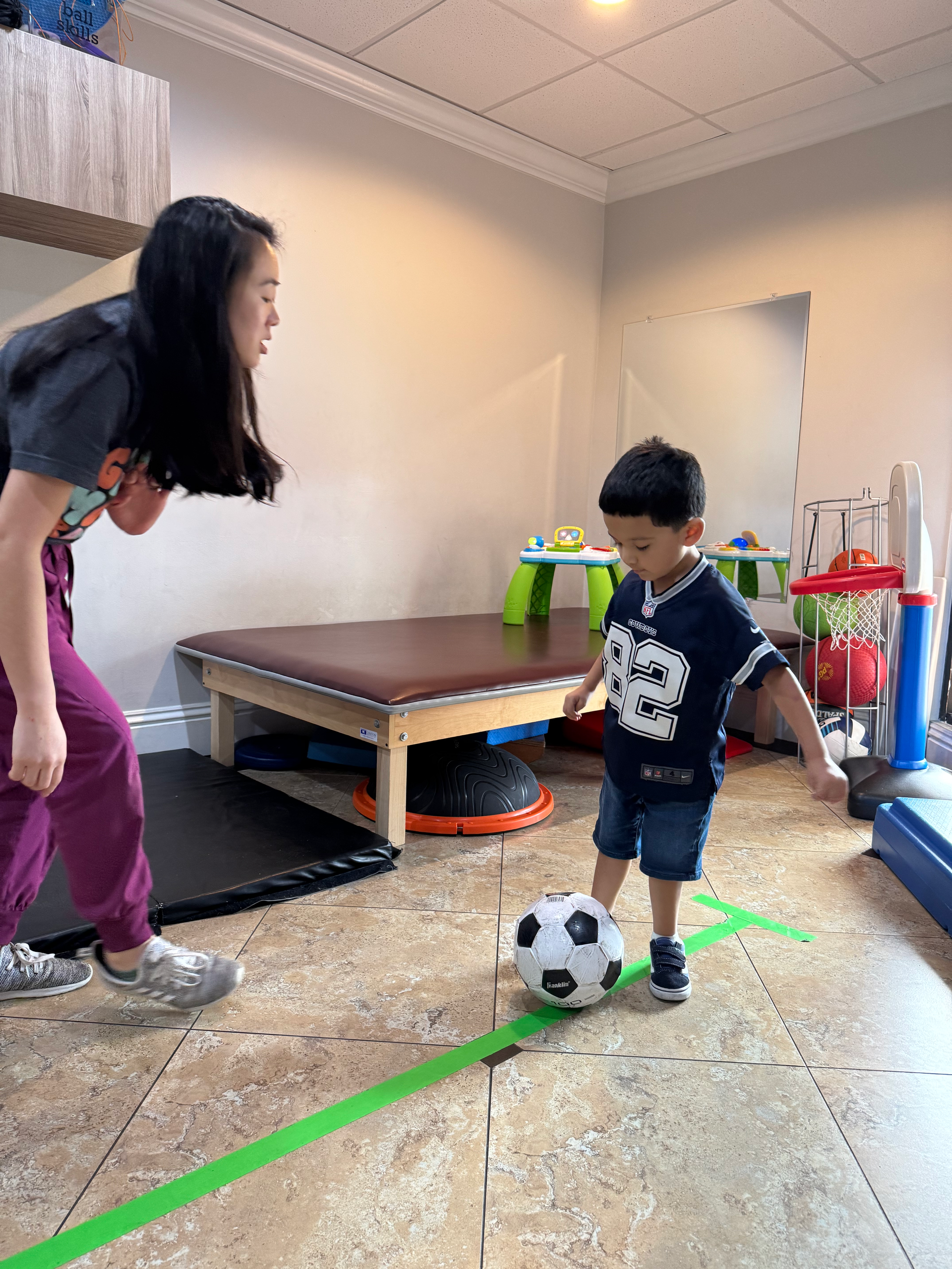 Adult and child playing with a soccer ball in a room with a bench and toys.