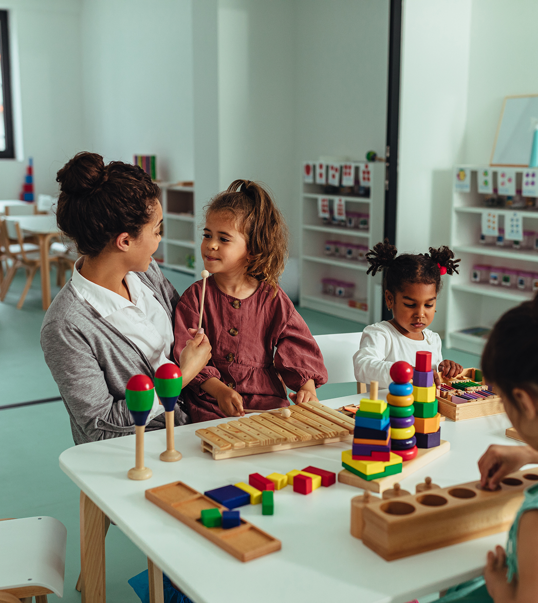 Children and a teacher at a table playing with colorful educational toys in a classroom
