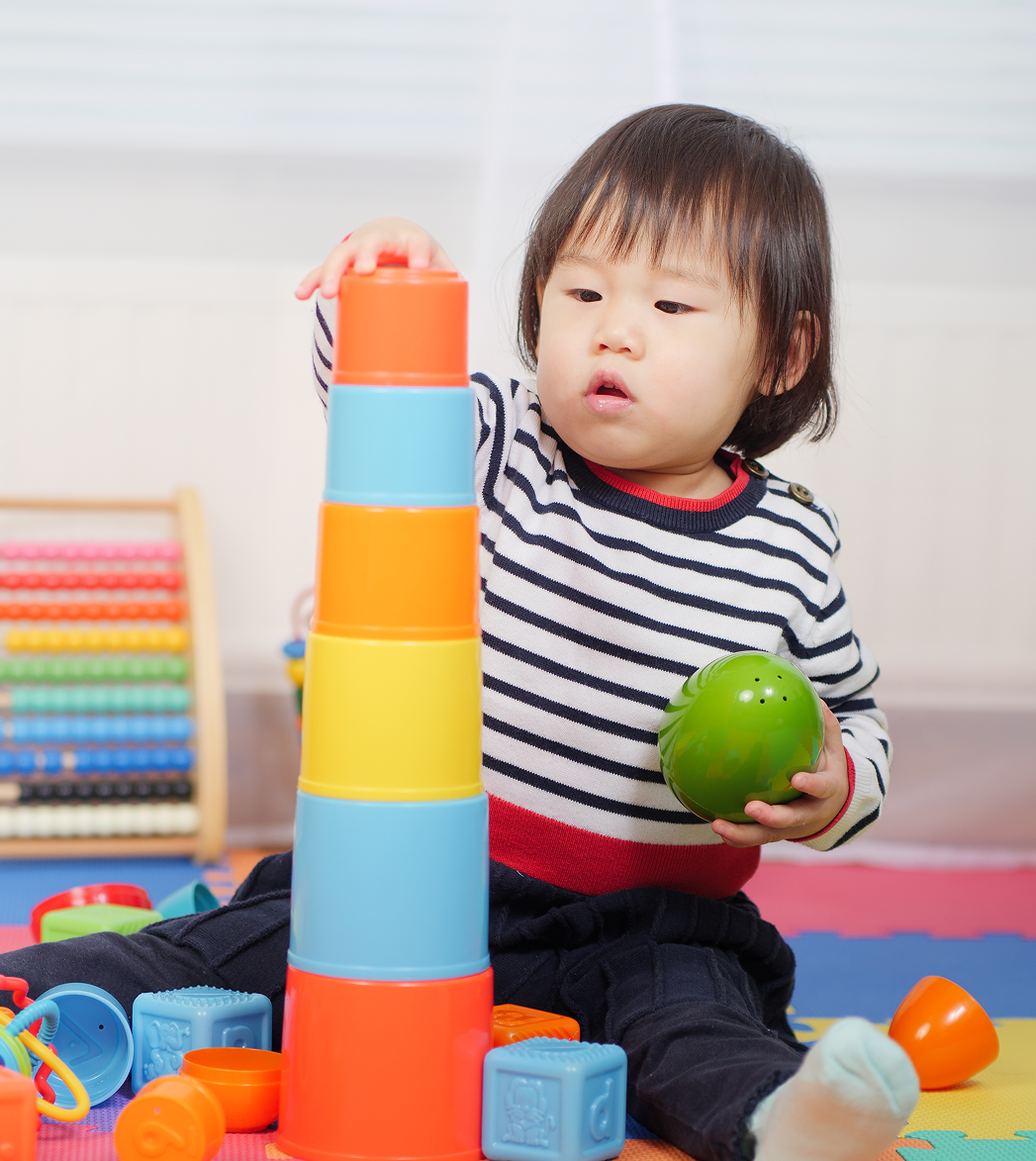 Child playing with colorful stacking cups and a green ball on a play mat