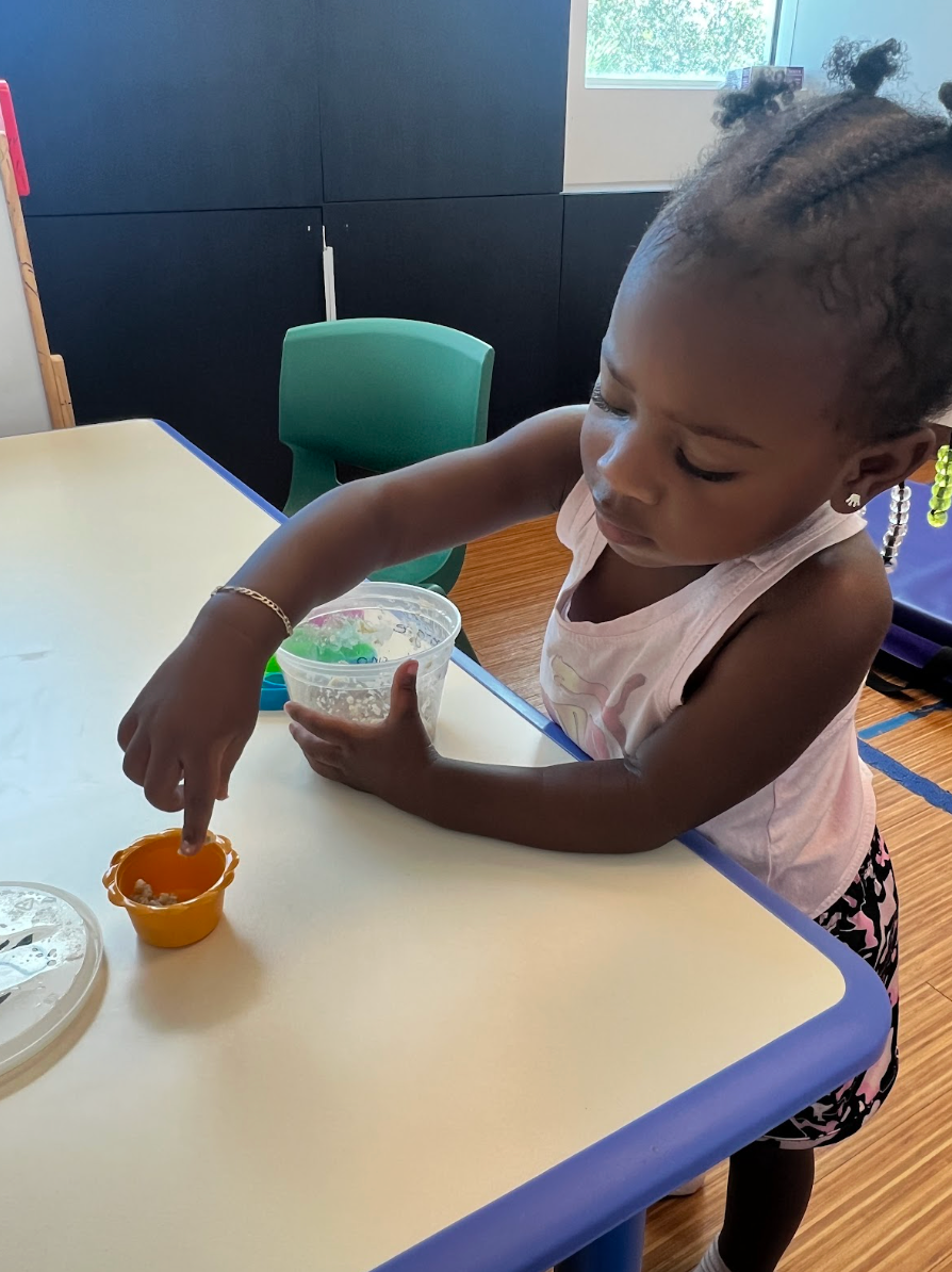 Toddler eating carrot sticks at a table, wearing a blue checkered shirt, with food in the foreground