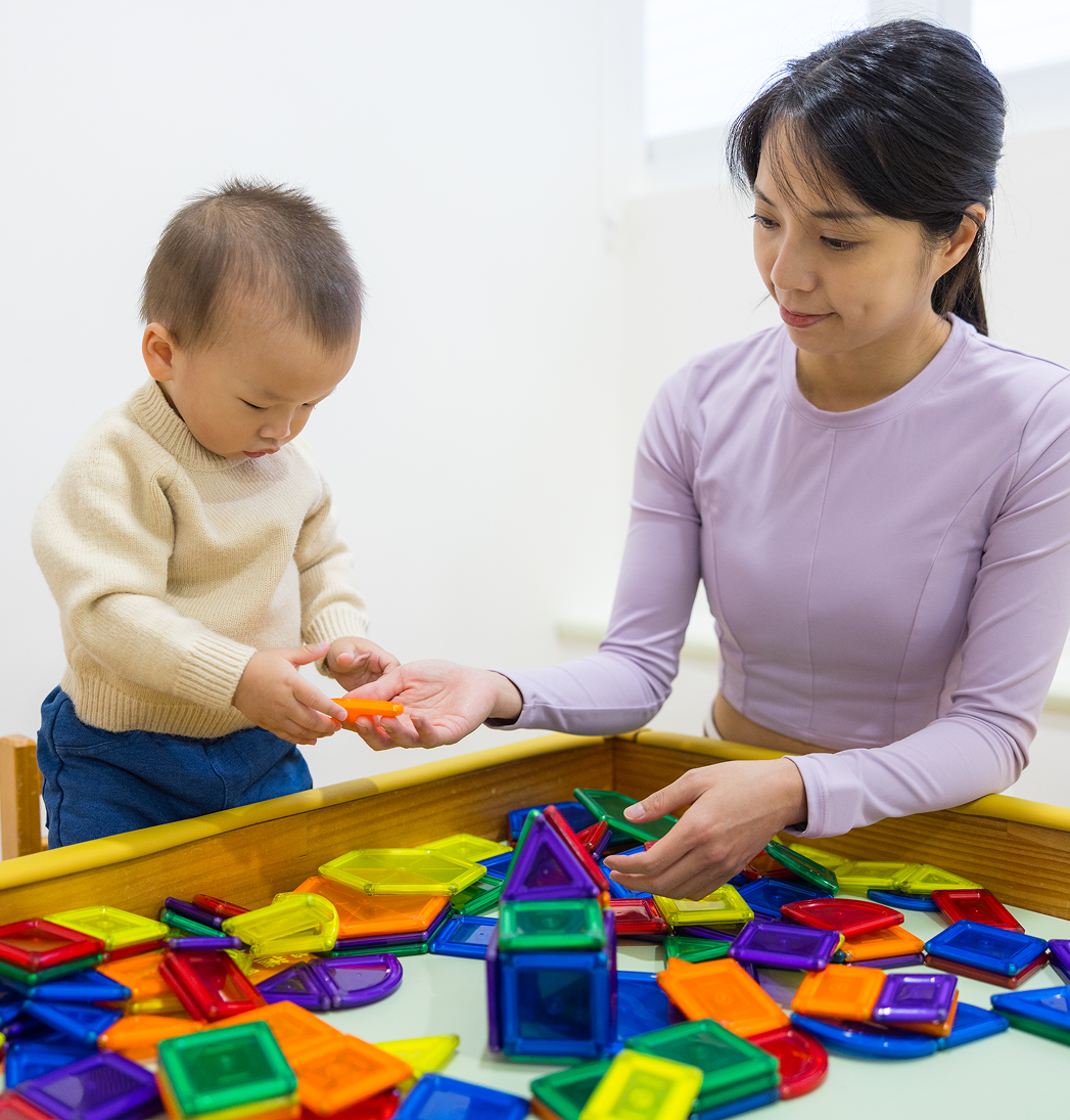 Adult and toddler sharing colorful magnetic blocks at a play table